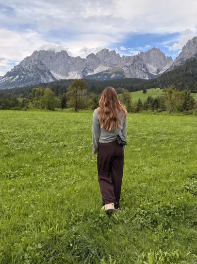 Nadine Stievermann von hinten auf einer Wiese, vor ihr Wald und Berge