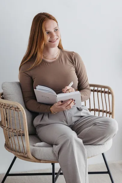 Nadine Stievermann sitzt lächelnd in einem Rattansessel und schreibt in ein Notizbuch