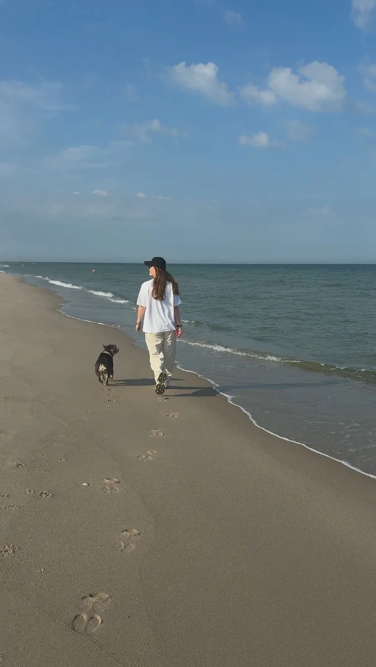 Nadine Stievermann von hinten bei einem Strandspaziergang mit ihrem Hund, hinter ihnen Fußspuren im Sand