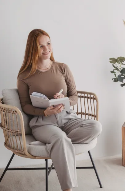 Nadine Stievermann sitzt in einem Rattansessel und schreibt in ein Notizbuch