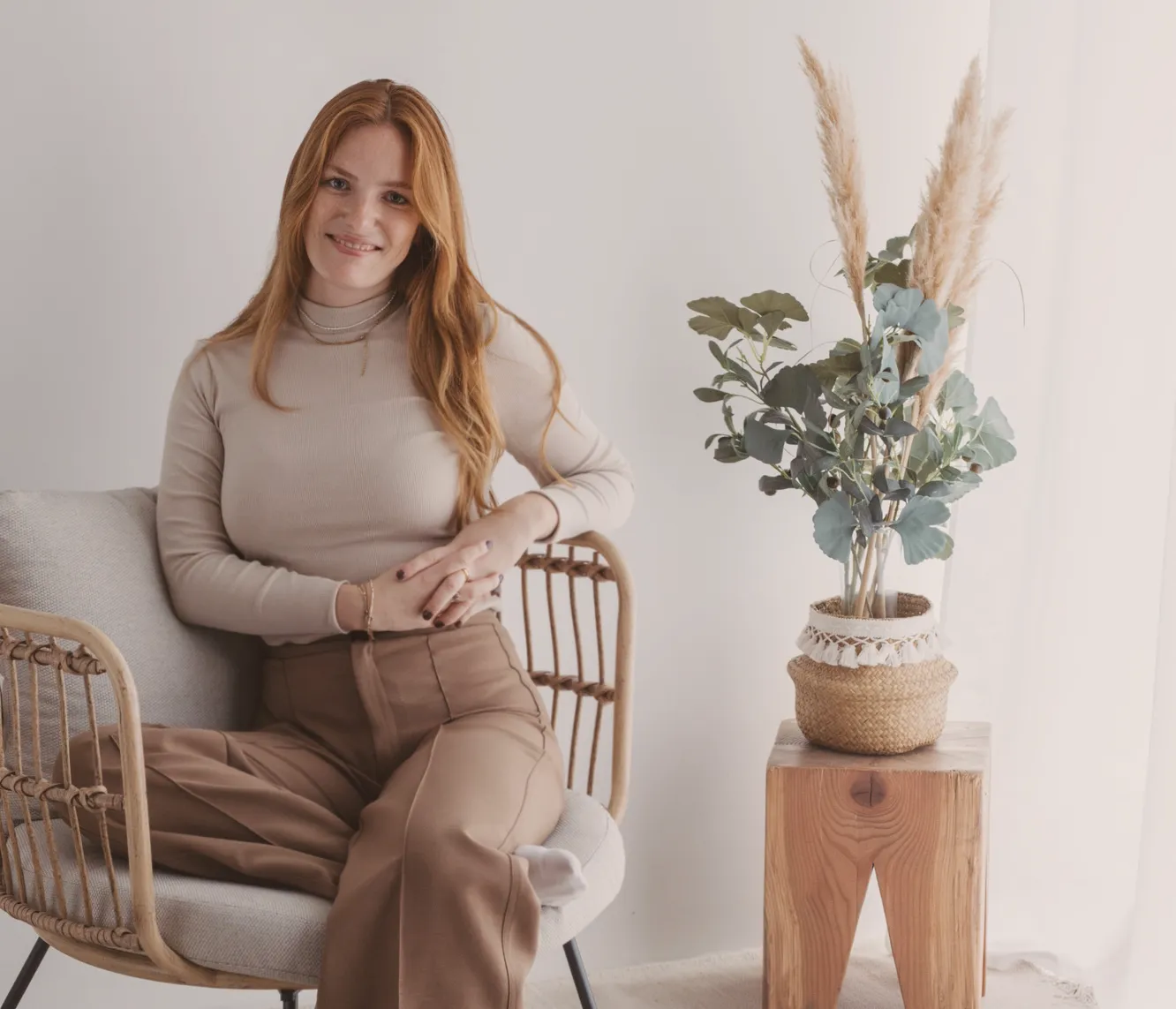 Nadine Stievermann sitzt lächelnd in einem Rattansessel neben einem Beistelltisch mit Trockenblumen